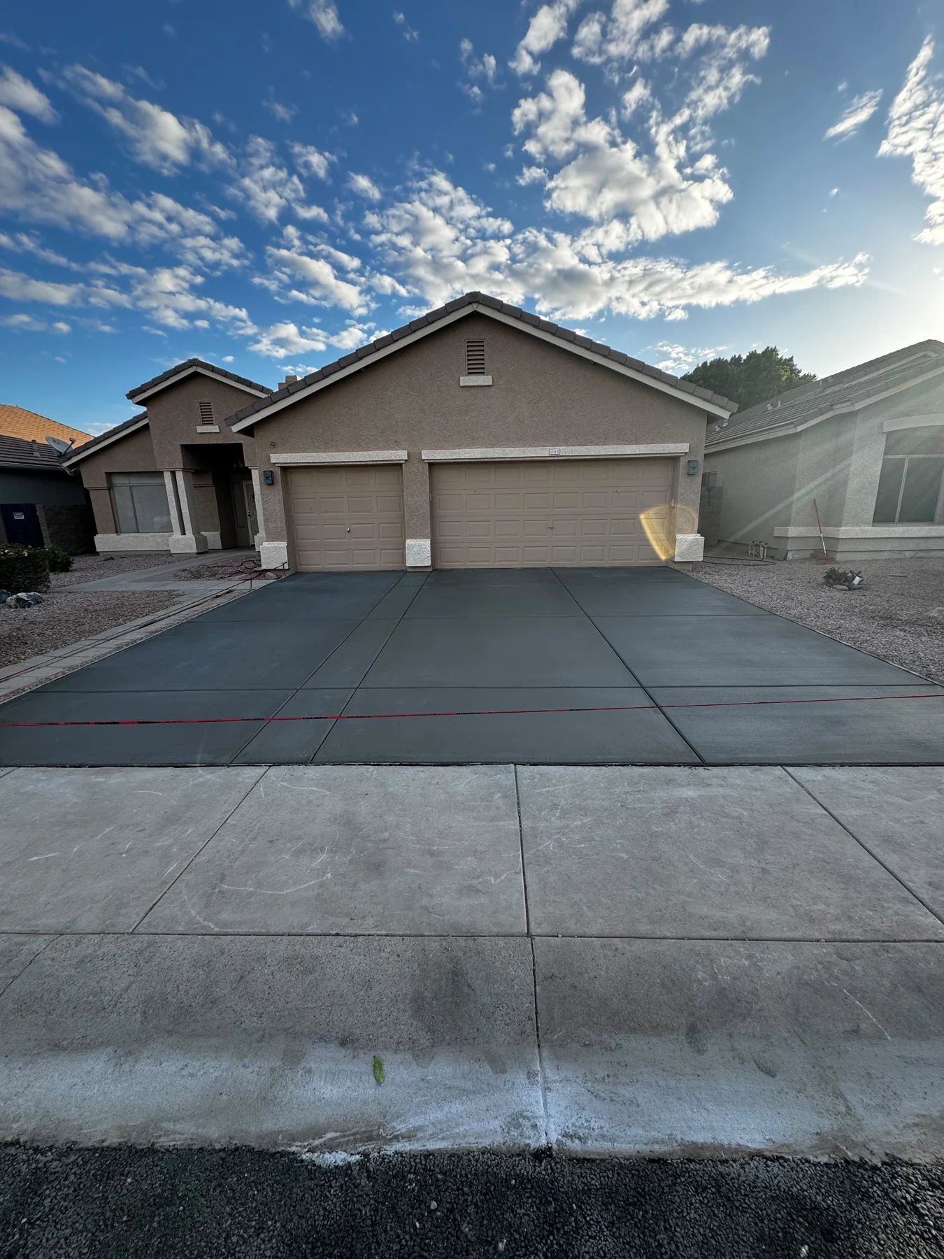 Completed concrete driveway leading to a residential garage under blue skies